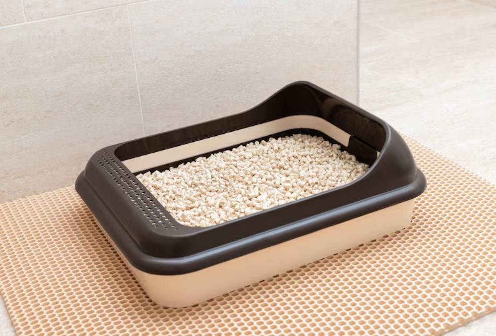 A modern cat litter box with beige and brown design, filled with white litter, placed on a textured mat in a tiled room.