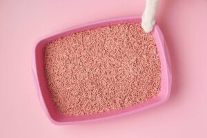 A pink cat litter box filled with light pink litter, with a cat's paw reaching in from the top.