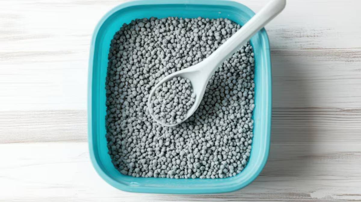 A turquoise container filled with small, round gray pellets, accompanied by a white scoop resting on top.