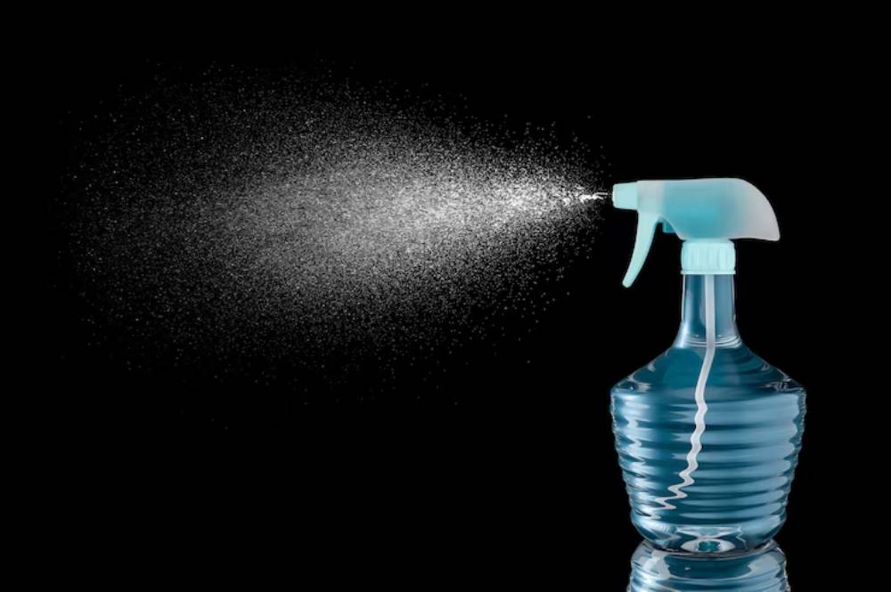 A blue spray bottle releases a fine mist against a black background, capturing the essence of cleaning and freshness.